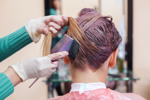 The hairdresser paints the woman's hair in white, apply the paint to her hair in the beauty salon.